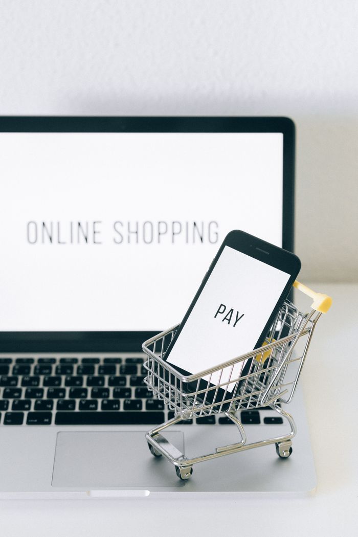 creative-01 A smartphone in a miniature cart on a laptop symbolizes online shopping and digital payment.